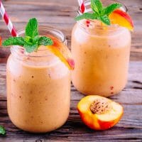 Healthy nectarine smoothies in a mason jar with mint on wooden background.