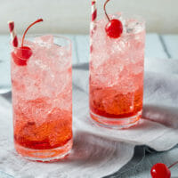 A Shirley Temple cocktail with ice cubes and a garnish of cherry.