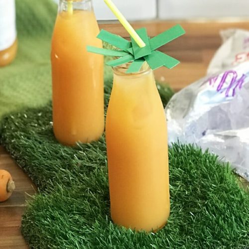 Carrot juice mixed with orange juice in a milk bottle style glass served over large ice cubes.