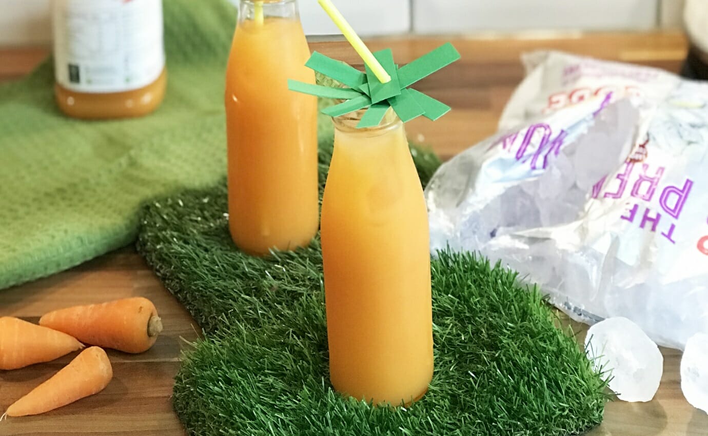 Carrot juice mixed with orange juice in a milk bottle style glass served over large ice cubes.