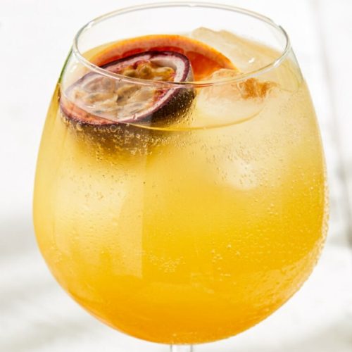 An iced called passionfruit spritz made in a large wine glass.
