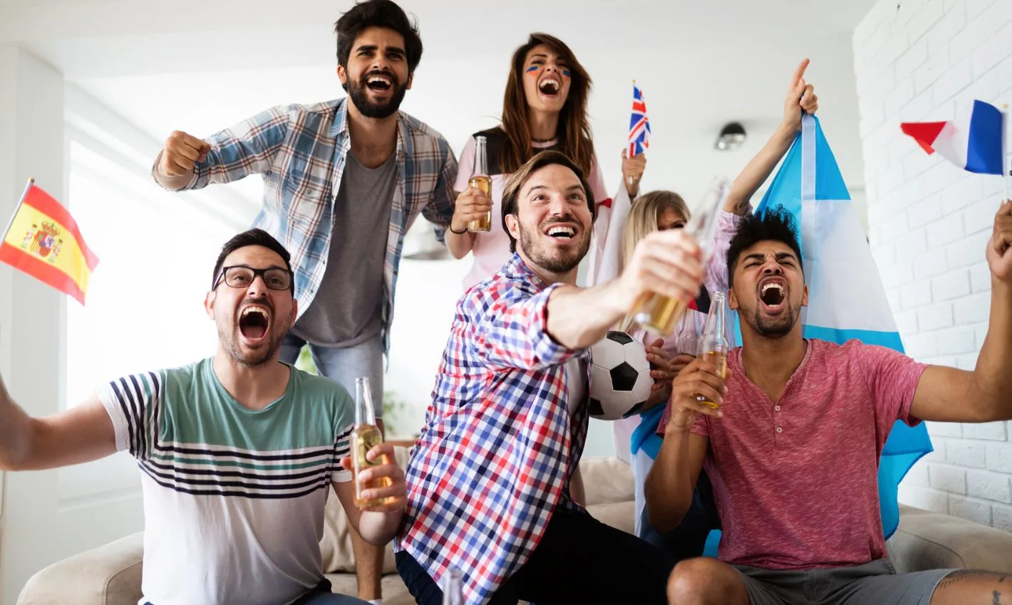 Diverse mix of friends sports fans watching winning football match on TV at home Celebrating winning goal