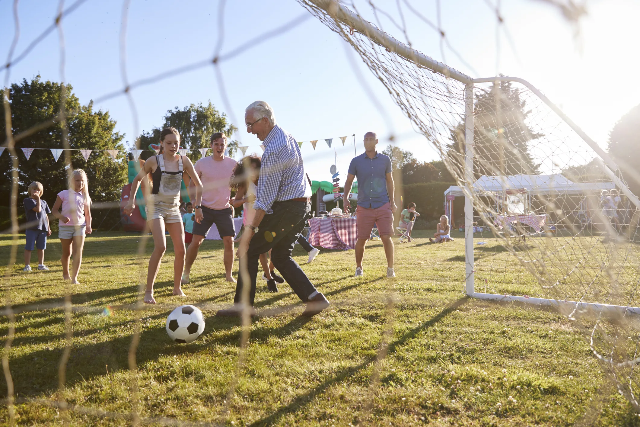 Children Playing Football Match With Father And Grandfather At Summer Garden Party