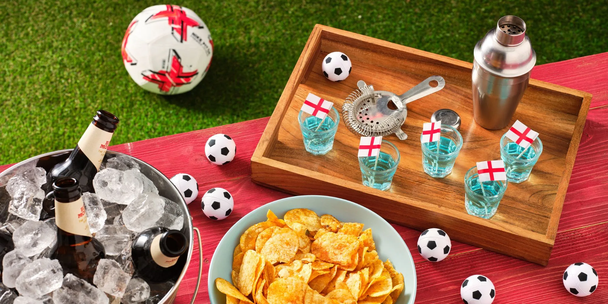 Beer bottles in an ice bucket next to a bowl of crisps, mini footballs and colourful shot drinks