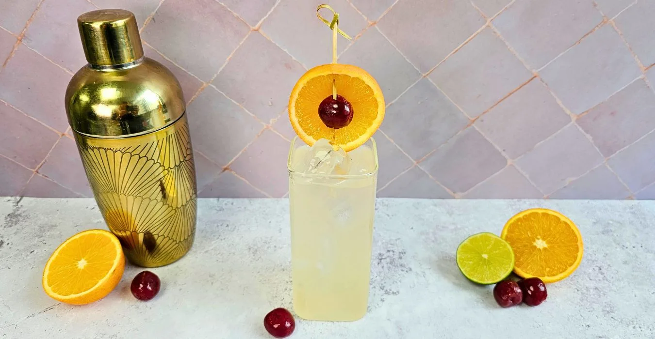 moscow mule mocktail next to a cocktail shaker and citrus fruit with a pink tile background