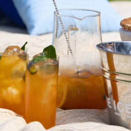 Alcohol Free Blueberry & Mint Iced Tea Sharer on a picnic blanket with an ice bucket and a picnic basket