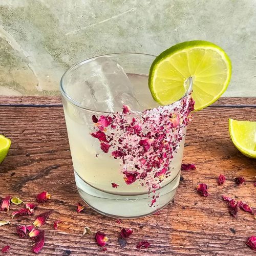 Elderflower & Rose Margarita surrounded by rose petals on a wooden table