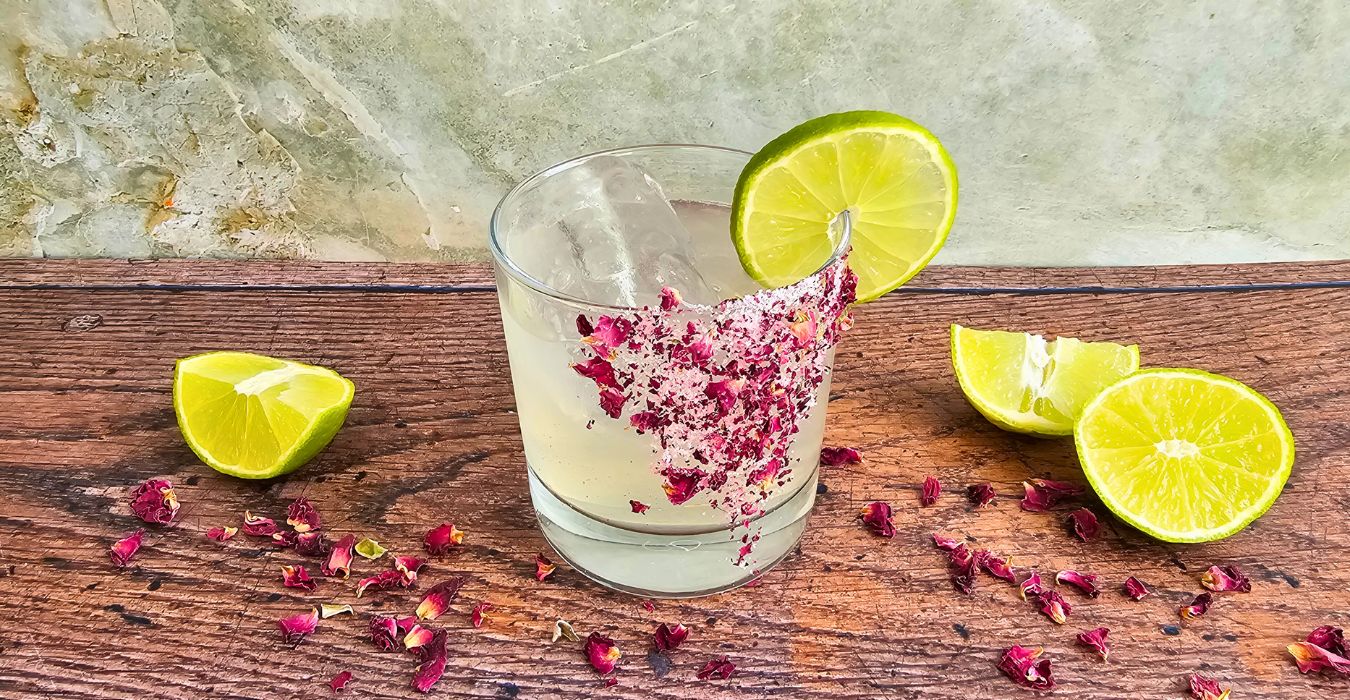 Elderflower & Rose Margarita surrounded by rose petals on a wooden table