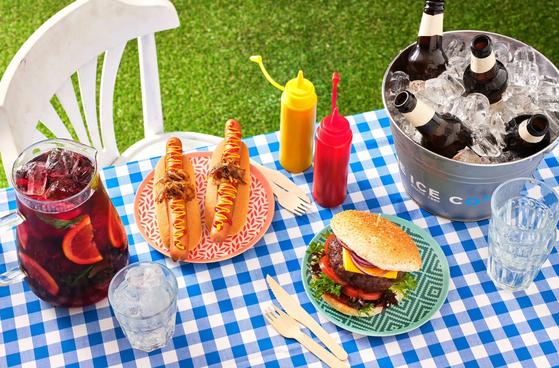bottles of beer chilling in an ice bucket, next to bbq food and a jug of sangria