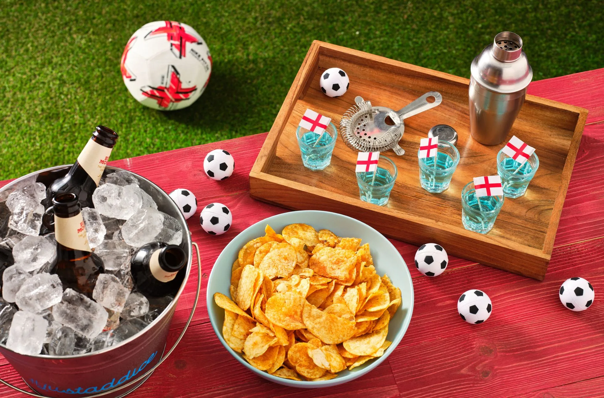 Beer bottles in an ice bucket next to a bowl of crisps, mini footballs and colourful shot drinks