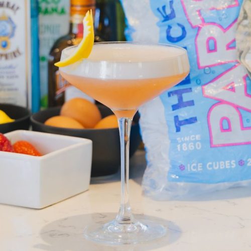 pink lady cocktail with a bag of party ice and bottles of gin