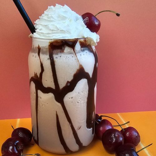 Lindt Indulgent Chocolate Milkshake topped with whipped cream, surrounded by cherries