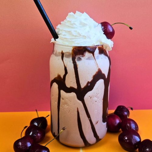 Lindt Indulgent Chocolate Milkshake topped with whipped cream, surrounded by cherries