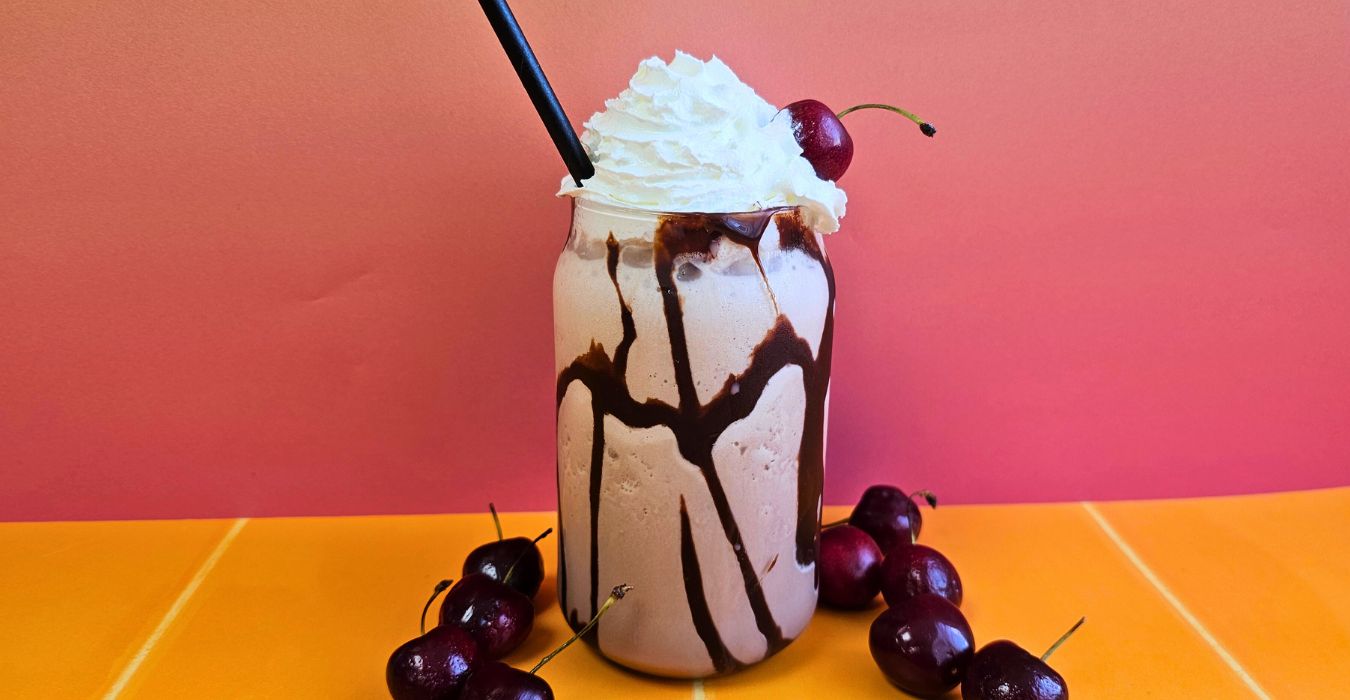 Lindt Indulgent Chocolate Milkshake topped with whipped cream, surrounded by cherries