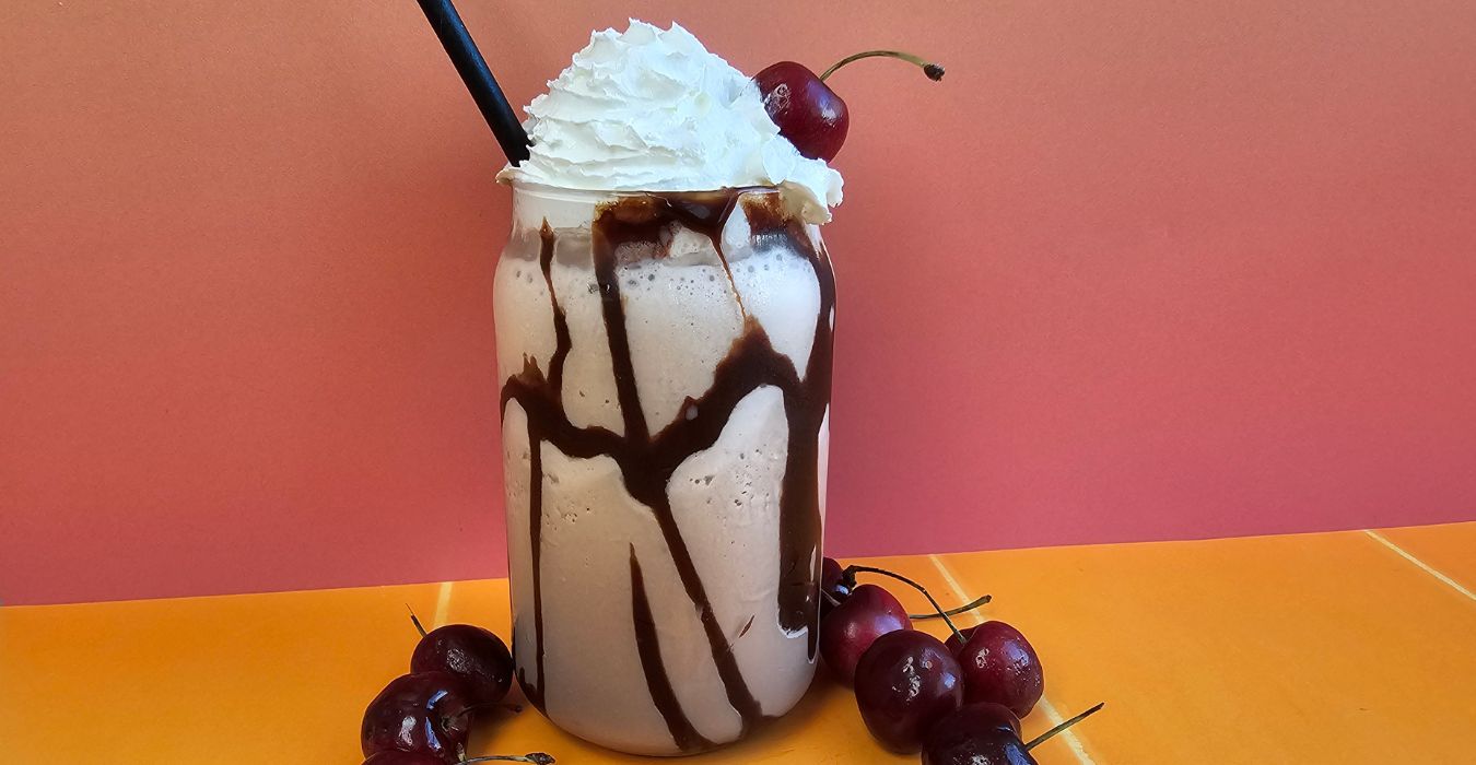 Lindt Indulgent Chocolate Milkshake topped with whipped cream, surrounded by cherries