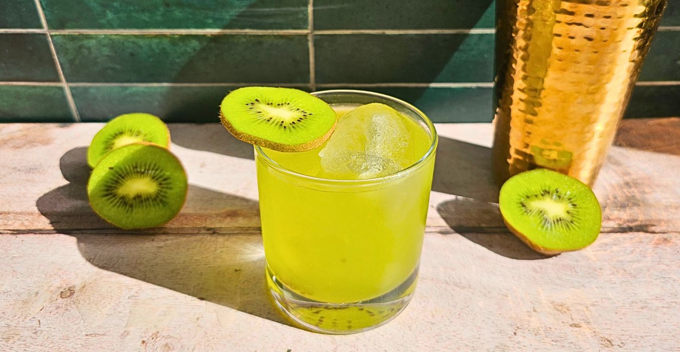 kiwiriqui cocktail next to a cocktail shaker and kiwi fruit