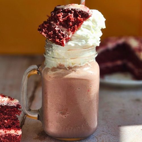 red velvet milkshake on a wooden table next to a slice of red velvet cake