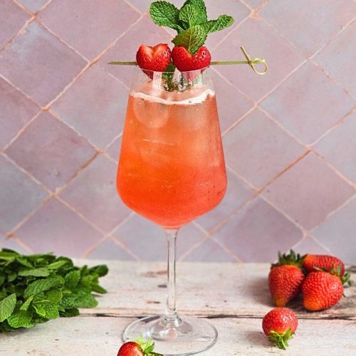 emily in paris rose spritz in a wine glass with fresh herbs and strawberries