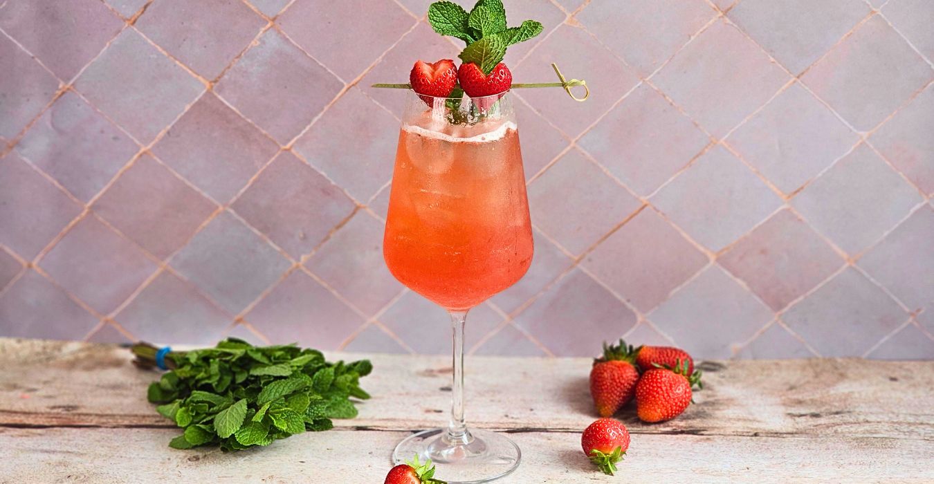 emily in paris rose spritz in a wine glass with fresh herbs and strawberries