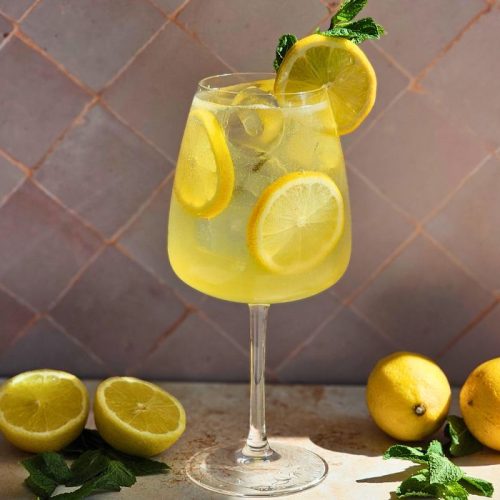 limoncello spritz cocktail in a wine glass surrounded by fresh lemons and mint