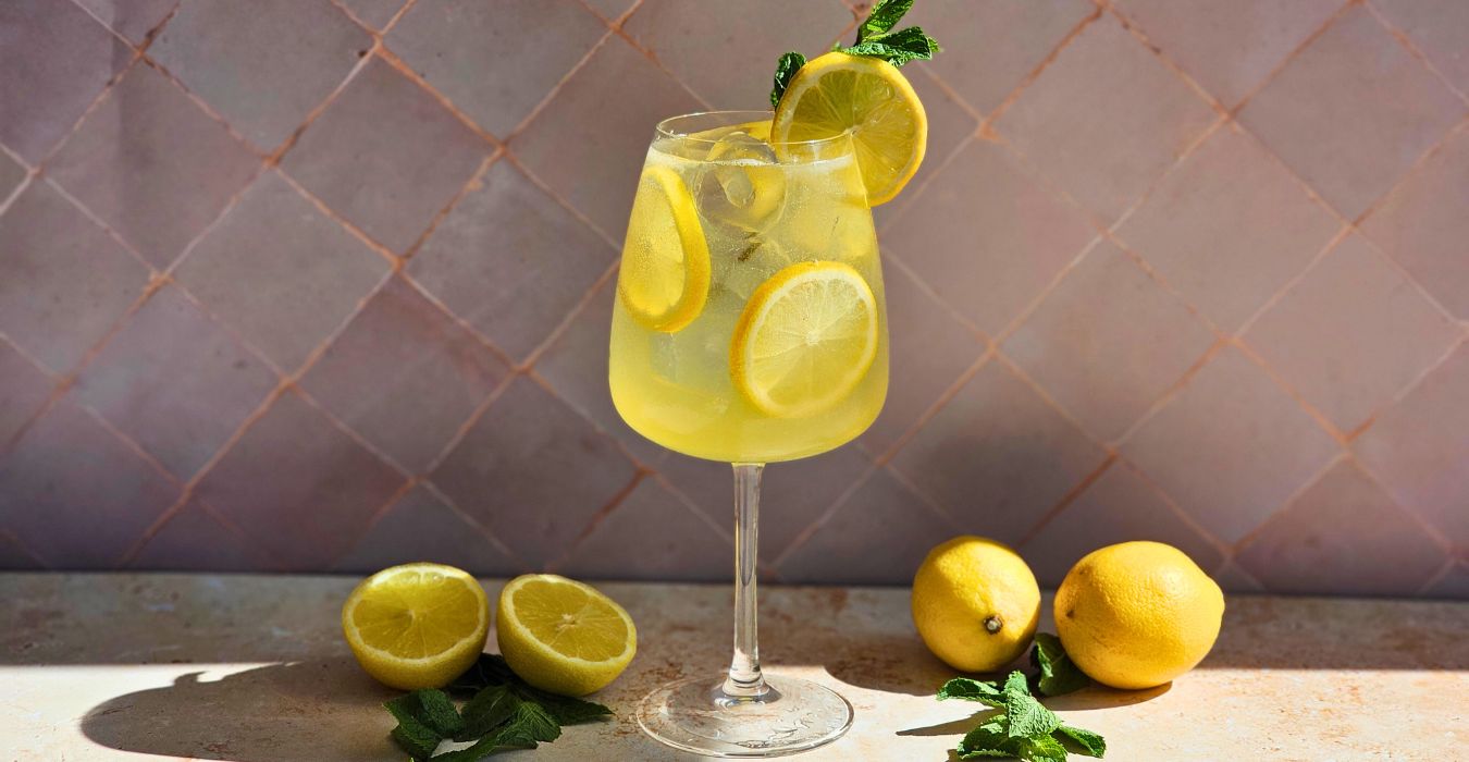 limoncello spritz cocktail in a wine glass surrounded by fresh lemons and mint