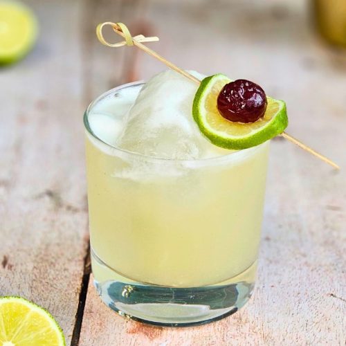 tequila sour cocktail with cherry and lime garnish on a wooden table