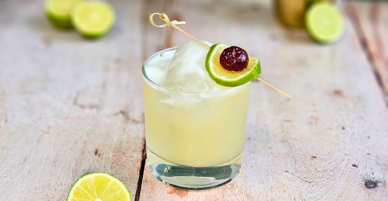 tequila sour cocktail with cherry and lime garnish on a wooden table