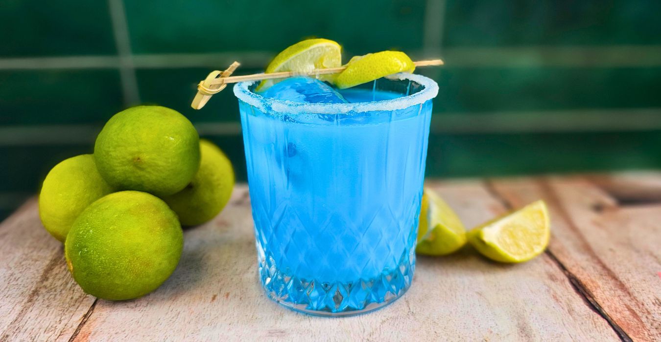 Blueberry Coconut Margarita cocktail next to pile of fresh limes