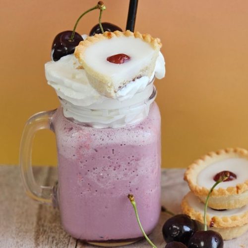 Cherry Bakewell Milkshake topped with whipped cream and a cherry bakewell garnish against an orange wall