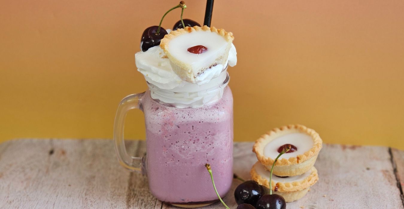 Cherry Bakewell Milkshake topped with whipped cream and a cherry bakewell garnish against an orange wall