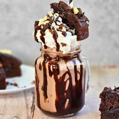 Chocolate fudge cake milkshake recipe topped with whipped cream and chocolate sauce with slices of chocolate fudge cake