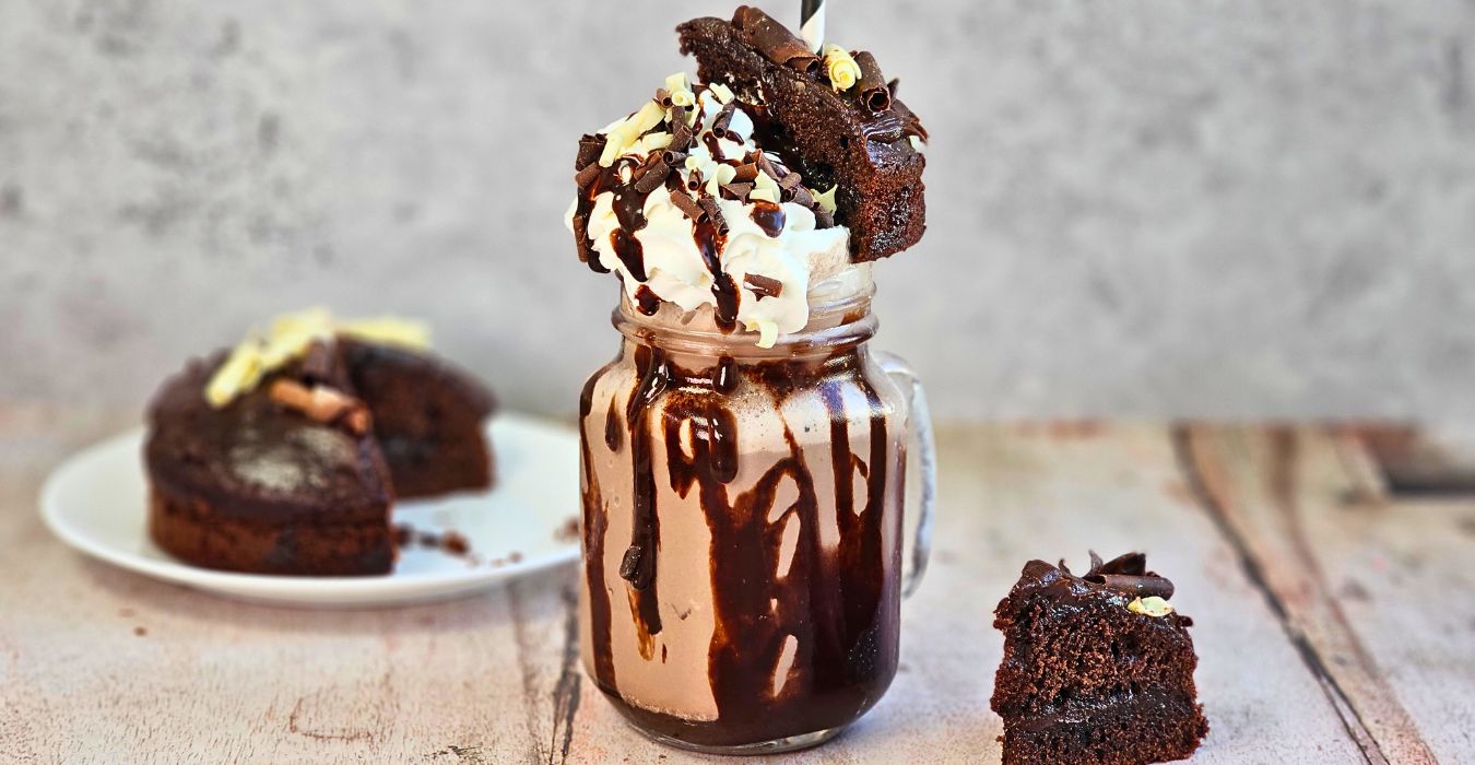 Chocolate fudge cake milkshake recipe topped with whipped cream and chocolate sauce with slices of chocolate fudge cake