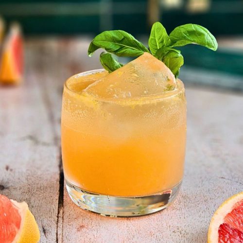 Elderflower Grapefruit Spritz Cocktail in a short glass next to fresh grapefruit and a sprig of basil