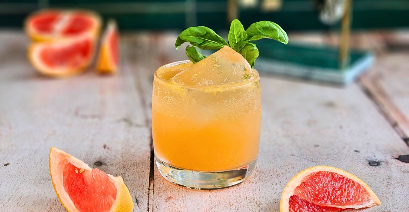 Elderflower Grapefruit Spritz Cocktail in a short glass next to fresh grapefruit and a sprig of basil