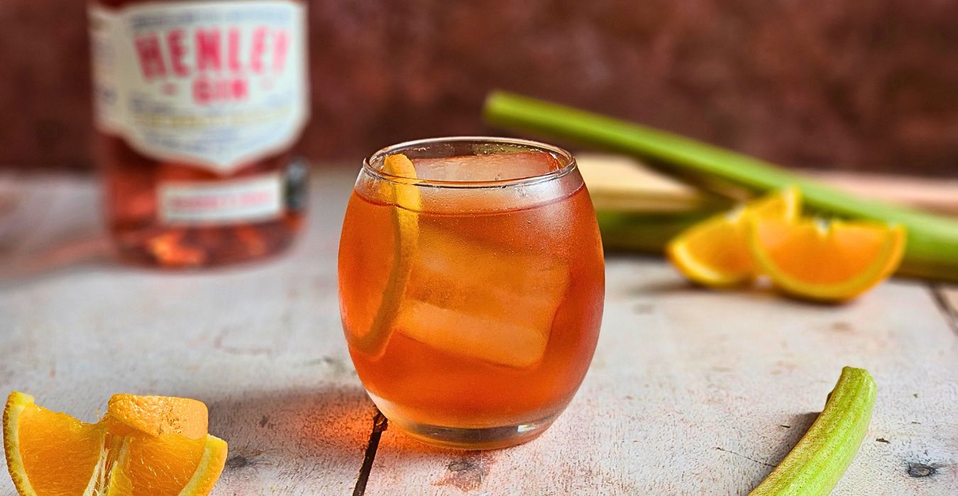 rhubarb and orange negroni fizz in a small round glass next to fresh orange slices and sticks of rhubarb