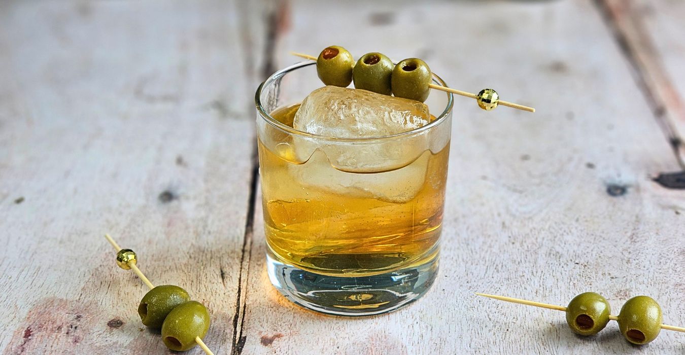 COconut Mezcal Spritz Cocktail Recipe garnished with stuffed olives in a rocks glass