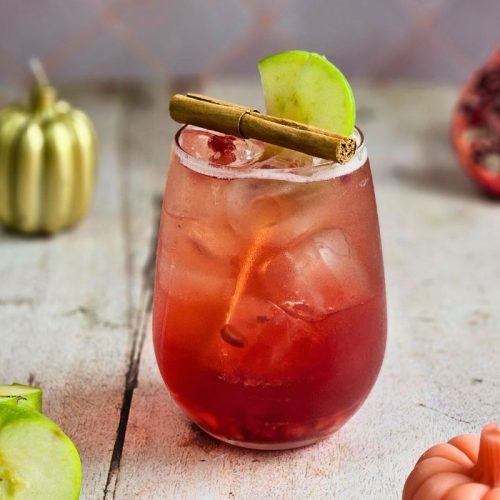 apple cider pomegranate spritz cocktail with autumn pumpkin candles and fresh pomegranate and apple fruits