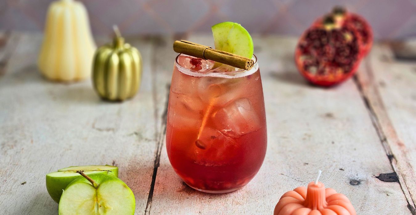 apple cider pomegranate spritz cocktail with autumn pumpkin candles and fresh pomegranate and apple fruits