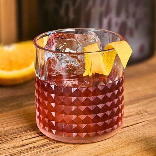 boulevardier cocktail with orange twist garnish on a wooden table with fresh orange slices