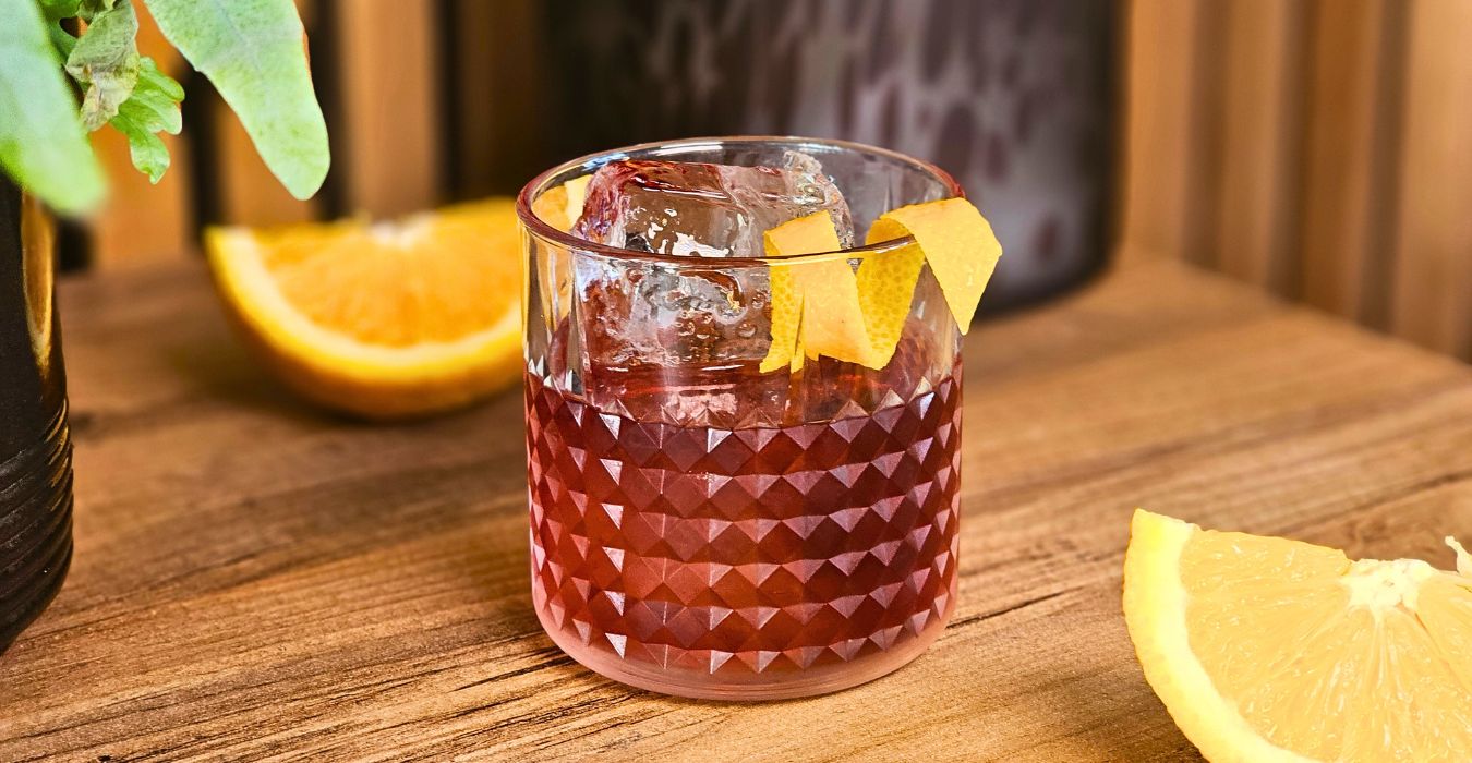 boulevardier cocktail with orange twist garnish on a wooden table with fresh orange slices