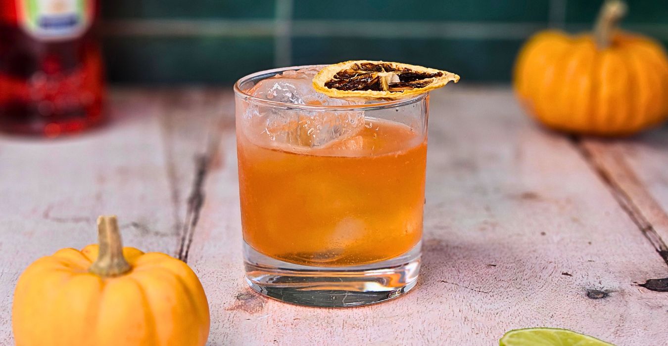 aperol pumpkin spice margarita cocktail in a short glass with tiny pumpkins