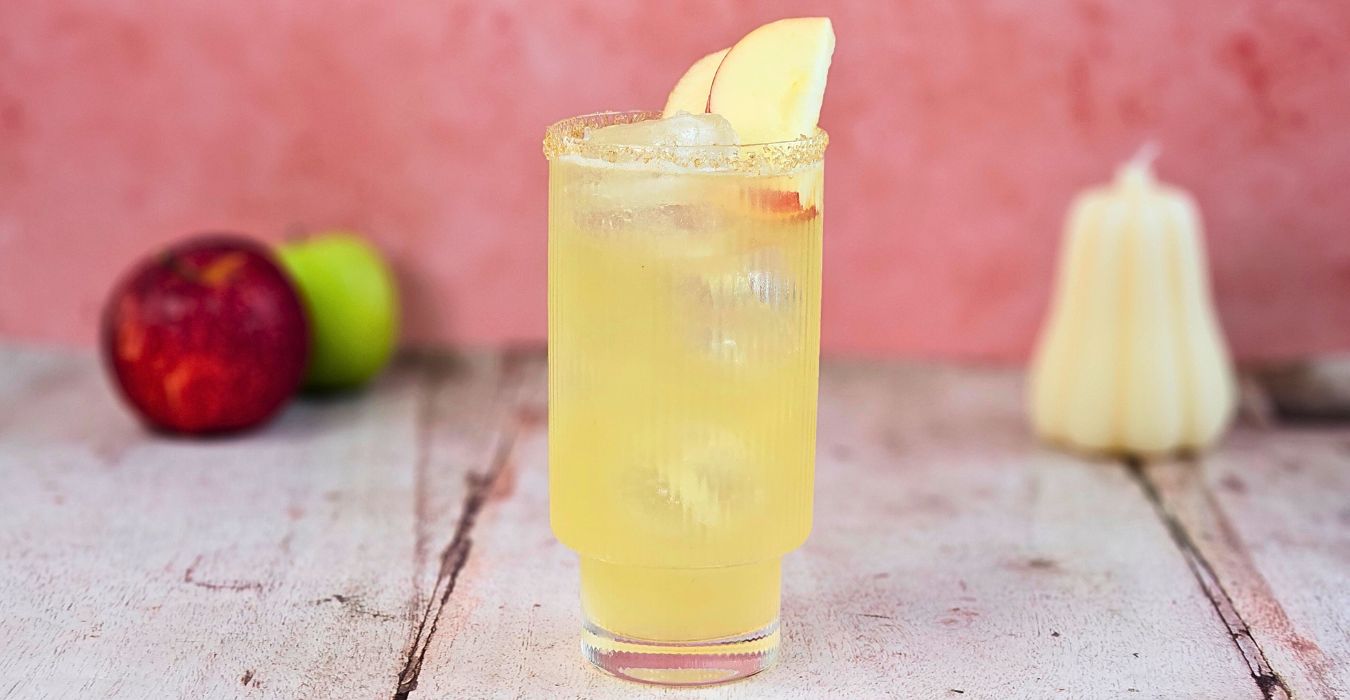 apple cider fizz mocktail cocktail in a tall glas with fresh apple and a sugar rim