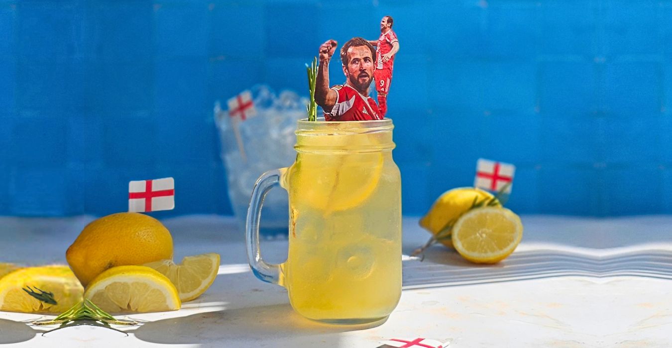 A beer cocktail in a glass garnished with a lemon slice and thyme, a Harry Kane inspired cocktail for the world cup with an image of him on a cocktail stick